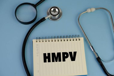 Üzerinde HMPV yazılı bir levha tutan eldiven giymiş bir sağlık görevlisinin resmi. Arka planda steteskop ve tıbbi maske var. İnsan metafnömotorirüsünün (HMPV) belirtileri ciddiyette değişebilir.