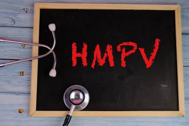 Üzerinde HMPV yazılı bir levha tutan eldiven giymiş bir sağlık görevlisinin resmi. Arka planda steteskop ve tıbbi maske var. İnsan metafnömotorirüsünün (HMPV) belirtileri ciddiyette değişebilir.