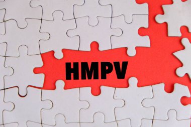 Üzerinde HMPV yazılı bir levha tutan eldiven giymiş bir sağlık görevlisinin resmi. Arka planda steteskop ve tıbbi maske var. İnsan metafnömotorirüsünün (HMPV) belirtileri ciddiyette değişebilir.