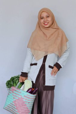 Sebzelerle dolu bir alışveriş çantası tutan genç Müslüman kadın.