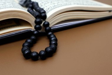 Kahverengi ahşap bir masada El Kuran ve dua boncukları açıldı.                        