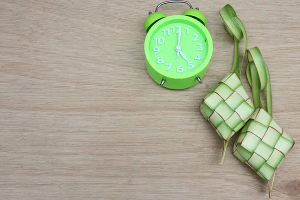 Yeşil alarm saati ve ketupat veya ahşap bir masada pirinç keki. Kurban Bayramı 'nda geleneksel Endonezya yemekleri                          