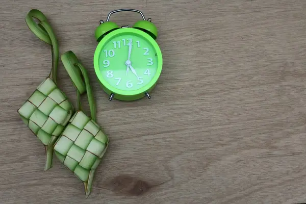 Yeşil alarm saati ve ketupat veya ahşap bir masada pirinç keki. Kurban Bayramı 'nda geleneksel Endonezya yemekleri                          