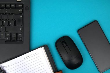 Dizüstü bilgisayardaki defter mavi masadaki akıllı telefonun yanında.