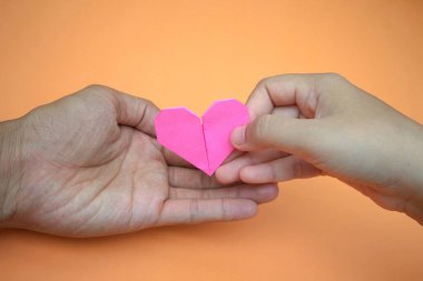 Pembe aşk şekilli origami kağıdını tutan bir kadının eli bir erkeğin eline teslim edilir.