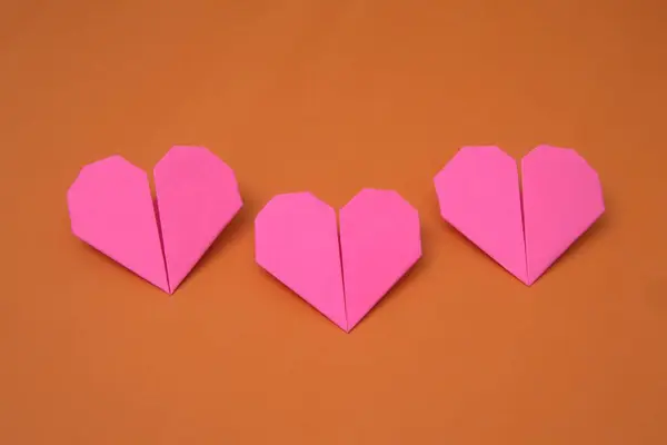 Bir grup origami kâğıdı pembe aşk şekilleri turuncu bir arkaplanda dizilmiş.                          