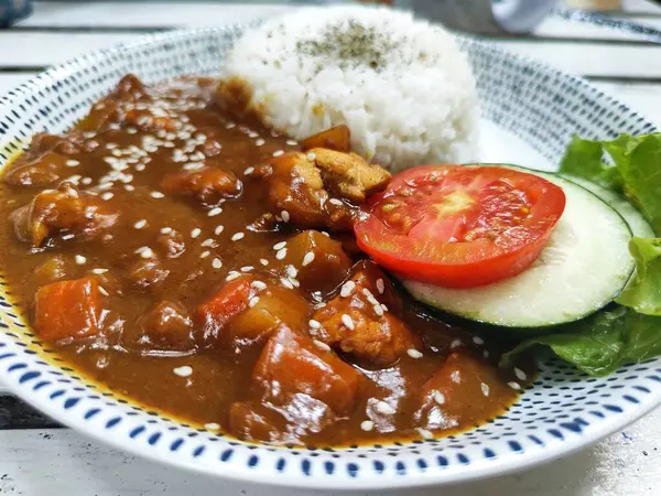 Tavuklu körili pilav ve beyaz tabakta servis edilen domates, salatalık ve marul.