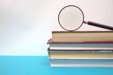 Büyüteç ve kitap yığını mavi masada.