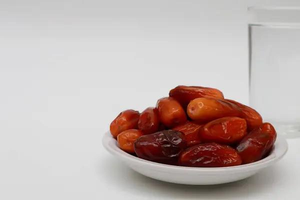 Bir bardak maden suyu ve beyaz arka planda bir tabak hurma.