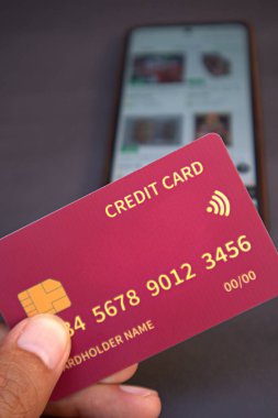 Adamın elinde cep telefonundaki internet dükkanının bulanık arkaplanlı kredi kartı var.