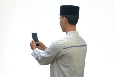 Asyalı Müslüman bir adam kameraya sırtı dönük bir cep telefonu tutuyor..