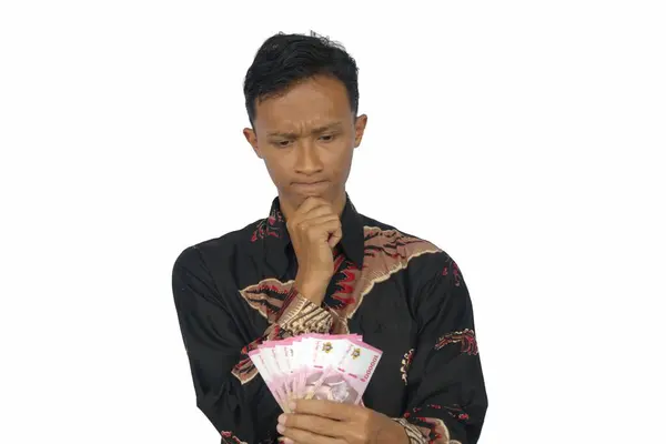 Asyalı bir adam, kafası karışık bir ifadeyle bir grup rupiah notası tutuyor.