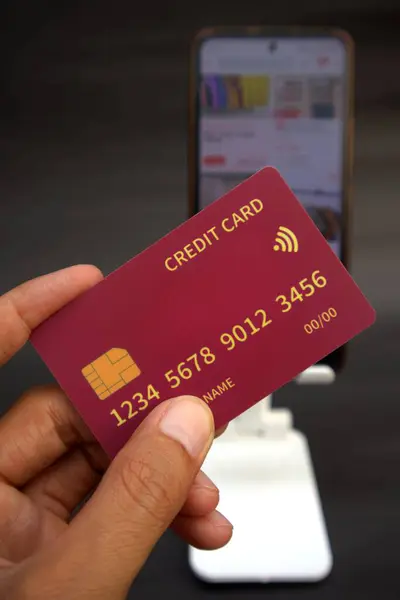 Adamın elinde cep telefonundaki internet dükkanının bulanık arkaplanlı kredi kartı var.