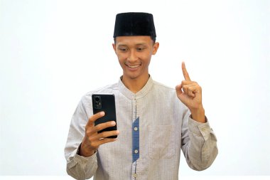 Asyalı Müslüman bir adam cep telefonu tutuyor ve mutlu bir yüz ifadesi göstermek için işaret parmağını kaldırıyor..