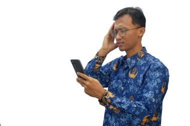 Endonezyalı devlet memuru üniforması giyen Asyalı bir adam elinde akıllı bir telefonla şaşkın ve şaşırmış bir ifade gösteriyor.