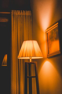 Bir lamba, duvara ve perdeye sıcak sarı bir ışık tutuyor. Sıcak ve davetkar bir atmosfer yaratıyor..