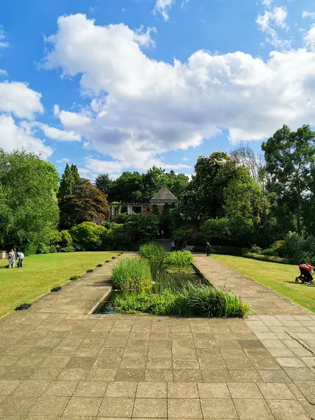 stock image Hampstead: view of the brick building surrounded by greenery. A small lake in the foreground. The Hill Garden and Pergola. Summer sunny day with clouds.