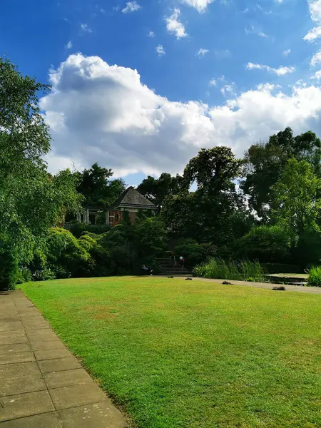 stock image View of the brick building surrounded by greenery. A small lake in the foreground. The Hill Garden and Pergola. Summer sunny day with clouds.