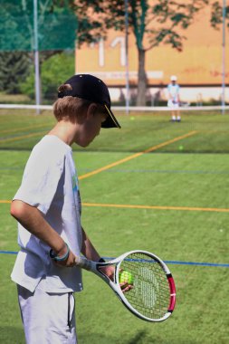 Yerel bir kortta tenis oynayan genç bir çocuk.