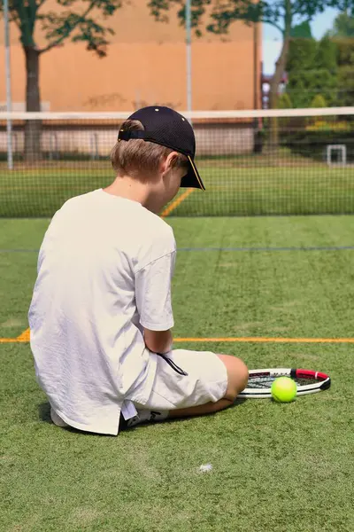 Yerel tenis kortunda tek başına oturan bir çocuk.