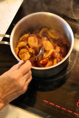 Bir tencereye erik döken ve erik reçeli hazırlayan yaşlı bir kadının eli.