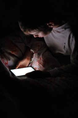 Çocuk gece yatağında akıllı telefonuyla oturuyor.