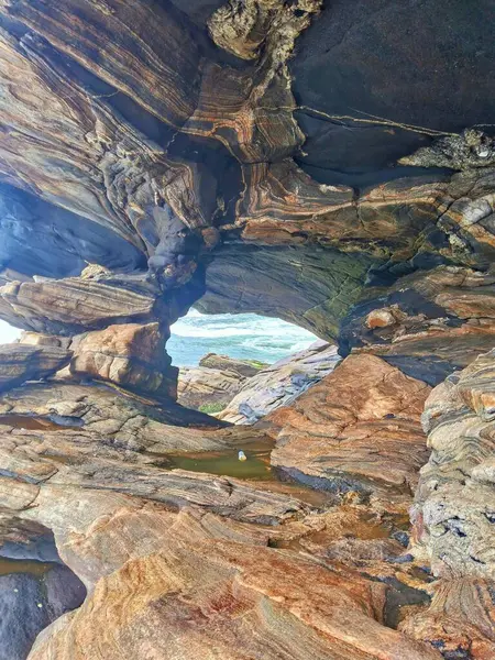 Arkasında deniz olan çeşitli renklerde bir taşın içindeki deliğin portresi.