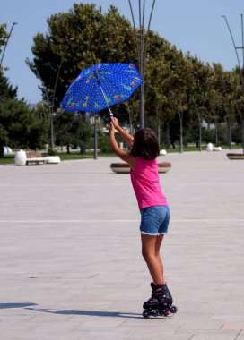Paten kayan kız parkta rüzgar ve şemsiyeyle oynuyor. Yüksek kalite fotoğraf