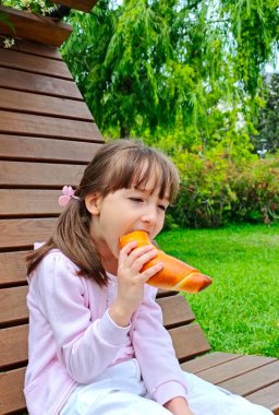 Küçük kız, parktaki çikolatalı çörekleri yiyor. 