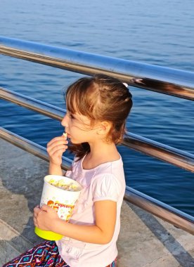 Küçük kız deniz kenarındaki parkta patlamış mısır yiyor. Yüksek kalite fotoğraf