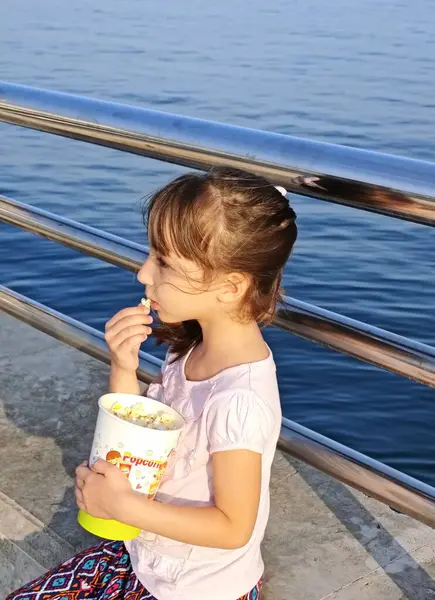 Küçük kız deniz kenarındaki parkta patlamış mısır yiyor. Yüksek kalite fotoğraf