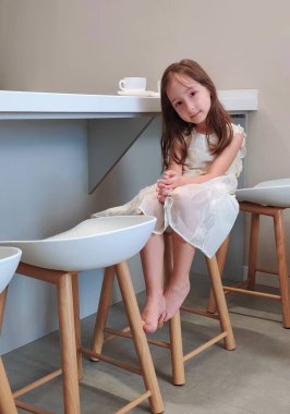 Kız mutfak masasında oturuyor ve kahvaltıyı bekliyor. Yüksek kalite fotoğraf