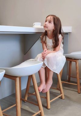 Kız mutfak masasında oturuyor ve kahvaltıyı bekliyor. Yüksek kalite fotoğraf