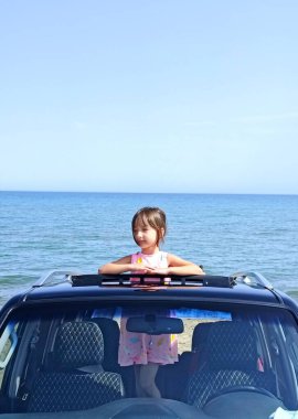 Küçük kız plajda arabanın ön camında duruyor. Yüksek kalite fotoğraf