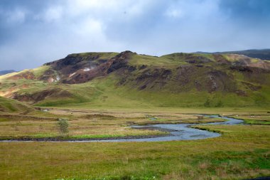İzlanda 'daki çarpıcı Yeşil Dağ Vadisi Çayırı' nda dramatik bulutlar ve içinden akan bir nehir var. Yüksek kalite fotoğraf