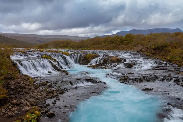 İzlanda 'da şelale, arkasında mavi su ve dağ var. Yüksek kalite fotoğraf