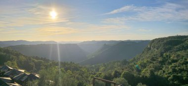 As the sun sets, the sun's rays descend over the valley of the mountains. A very wooded valley. The tops of some parasols. clipart