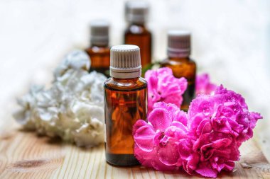 Several amber bottles filled with essential oil, arranged on a wooden surface with pink and white flowers beside them.