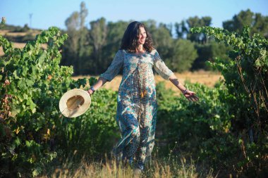 Güzel bir kadın bir demet şarapla tarlada yürüyor.