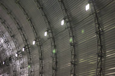 Kemerli, metal kaplı bir yapının içine ayrıntılı bir bakış, eşit aralıklı ışıkların kaburgalı panelleri aydınlattığı, ritim ve simetri duygusu yarattığı. Temiz çizgiler ve yapısal tasarım mimari hassasiyeti vurgular..