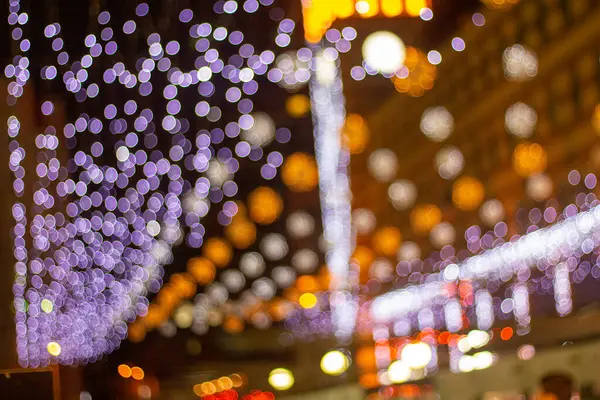 Gece gökyüzünü mor, beyaz ve turuncu renklerle dolduran büyüleyici bir bokeh ışık gösterisi büyülü bir ortam yaratıyor. Şehir, tatil neşesi ve sıcaklığıyla parıldıyor..