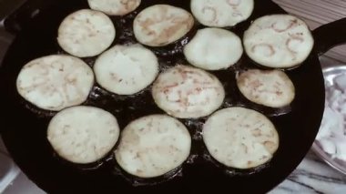 Patlıcan dilimleri (Solanum melongena) koyu, yuvarlak bir tavada kızartılır. Patlıcan dilimleri eşit düzenlenmiş ve hafif kahverengiye benzer şekilde yağ içinde cızırdıyor. Tawa görünür bir alevle birlikte sobanın üstünde.. 