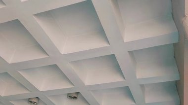 Beton ve çimentodan yapılmış bir iç tavan tasarımı, yapılandırılmış ve geometrik mimari bir görünüm oluşturan kare kutu benzeri aralıklardan oluşan bir ızgara deseni içerir.