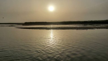 Güneş merkezli bir su kütlesinin üzerinde sakin bir günbatımı. Yüzeyde yansıması, sakin ve simetrik bir sahne yaratıyor.
