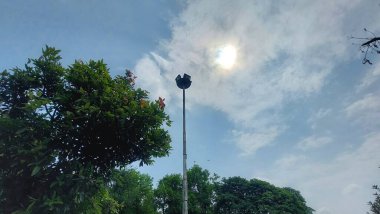 Ağaçlı ve bulutlu mavi gökyüzü olan uzun bahçe direğinin alçak açısı