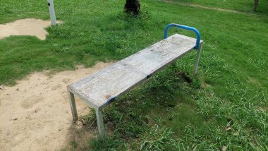 Kamu parkında mavi gidonu olan paslı oturma tezgahı.