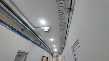 Endüstriyel tavan kanalları ve fayanslı zemin perspektifiyle aydınlık bir koridor.