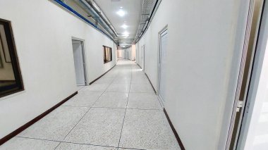 Endüstriyel tavan kanalları ve fayanslı zemin perspektifiyle aydınlık bir koridor.