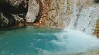 Beautiful waterfall base with crystal clear aquamarine pool and dramatic rocky cliffs