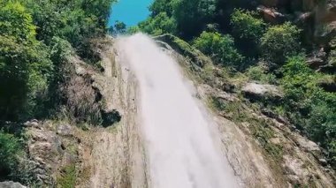 Majestic towering waterfall with frothy white cascade over rocky cliffs and clear blue sky